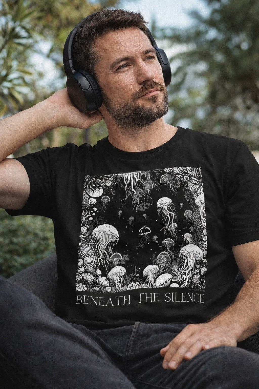 Male model wearing a black unisex monochrome jellyfish nautical graphic t-shirt while relaxing with over-ear headphones
