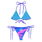 Back view of women’s ocean pink print recycled string bikini bottoms with pink and blue fluid art design and white circular The Naughty Angler™ logo